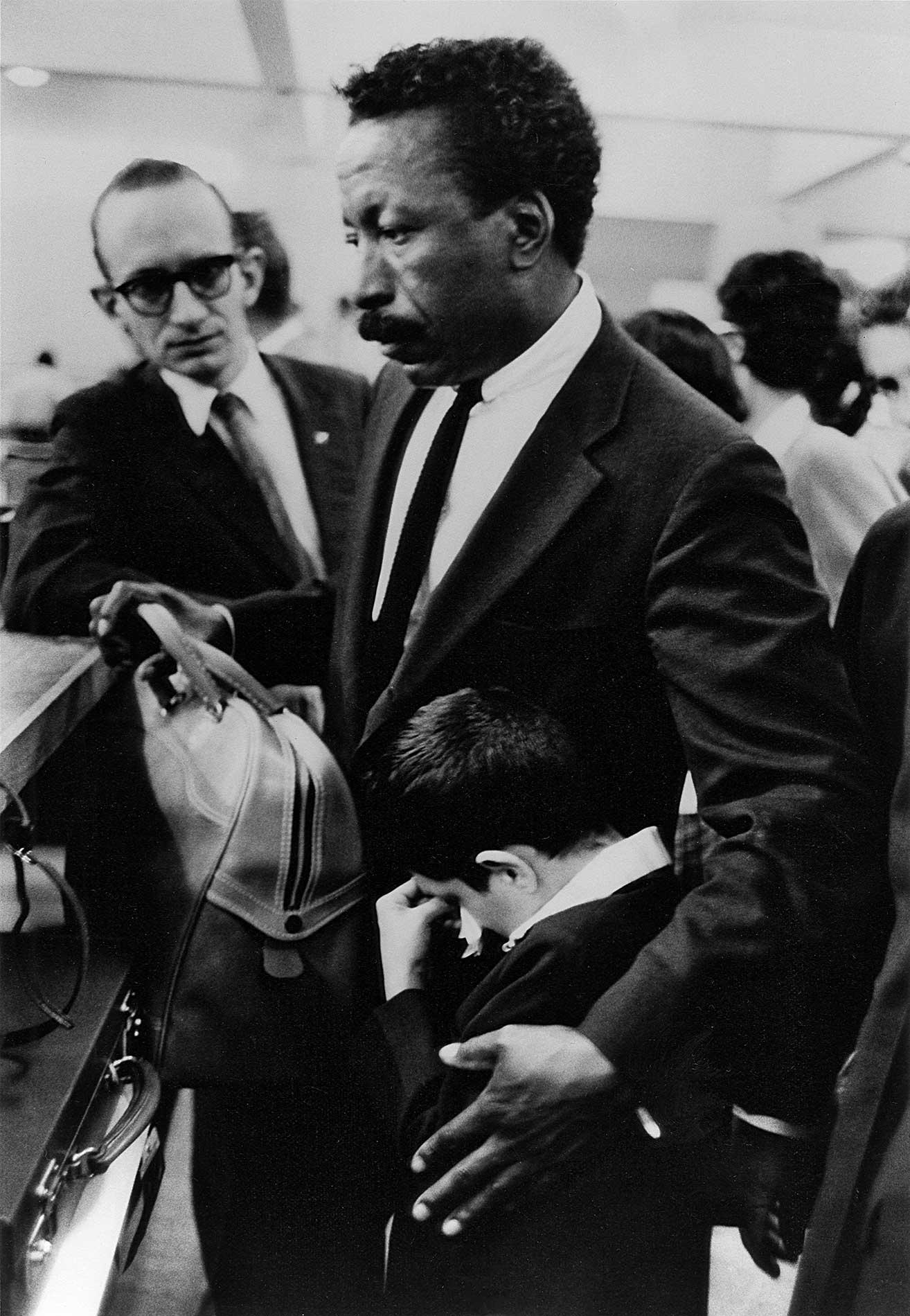 Gordon Parks standing with a little boy crying into his arms surrounded by cameras