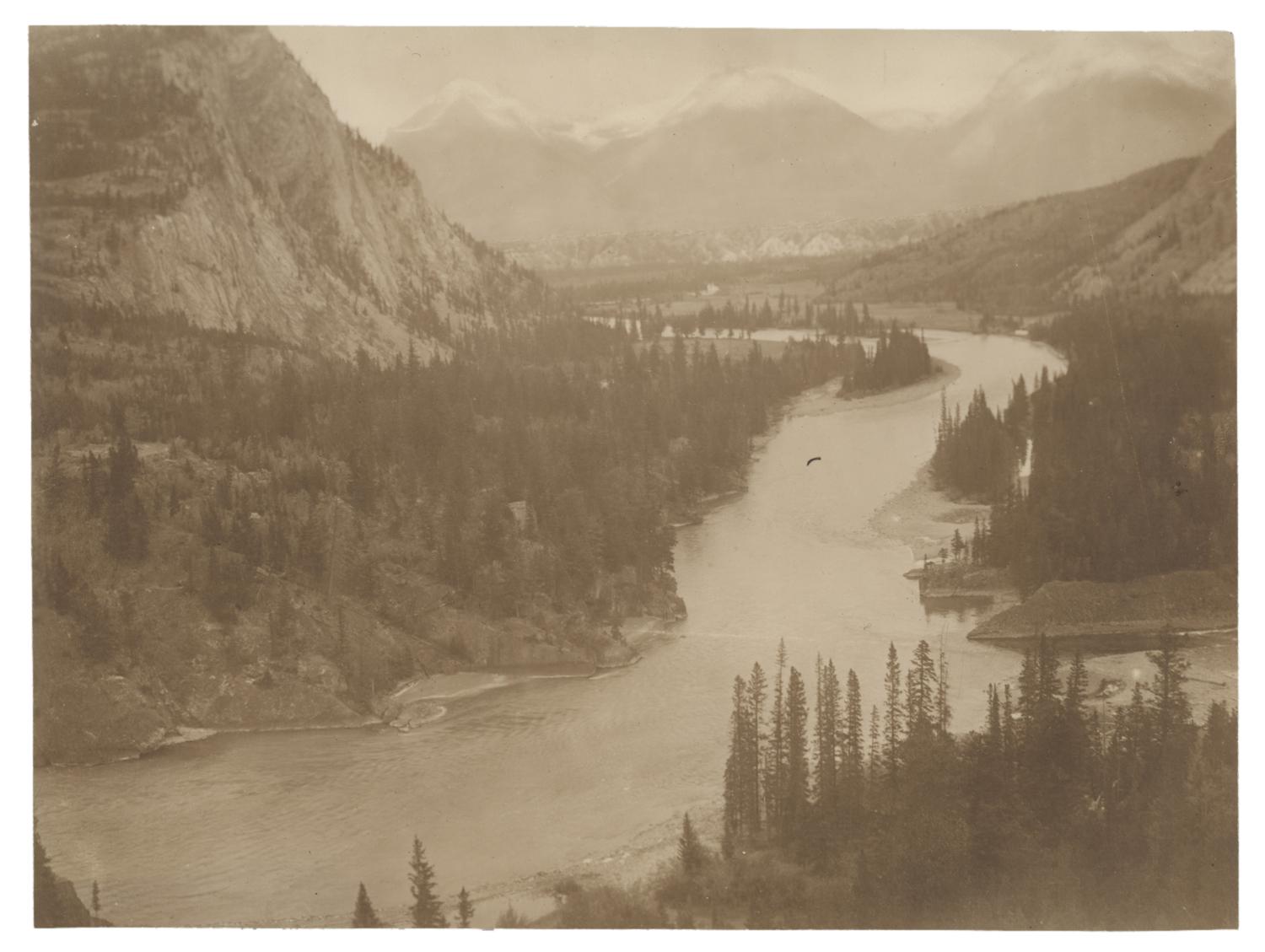 Landscape view of a river flowing through trees and mountains. Black and white photograph by Minna Keene.