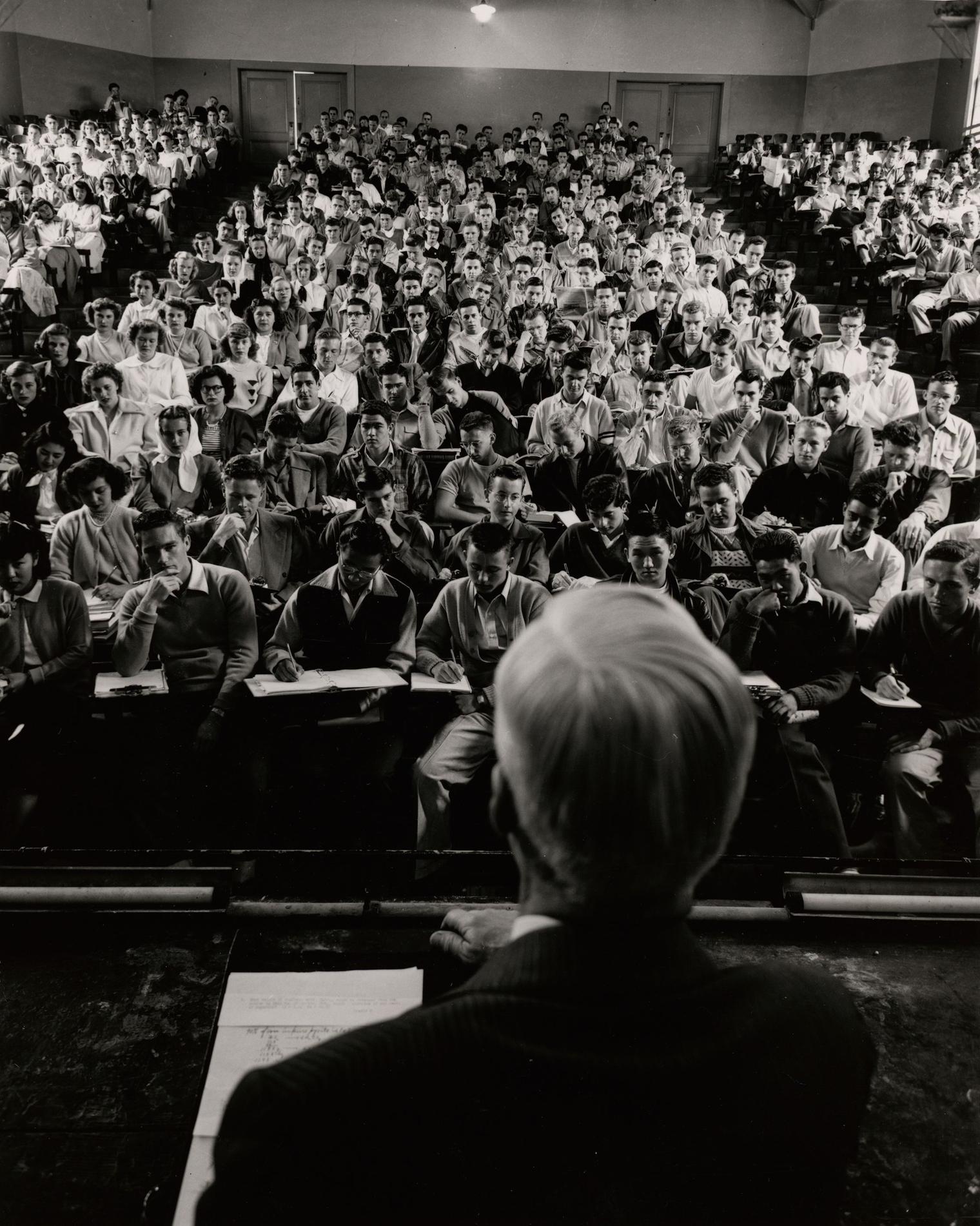A man at a podium looks out into an auditorium containing hundreds of people