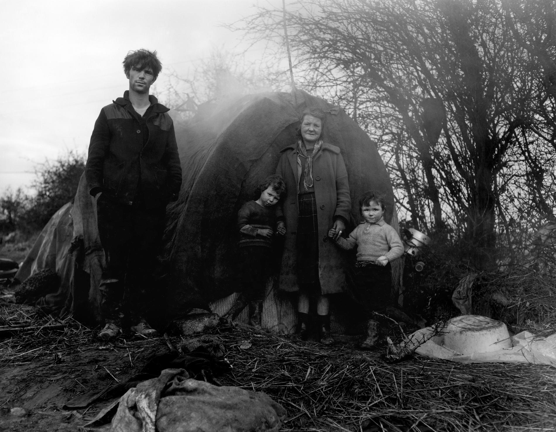 A family stands in a forest in front of a tent