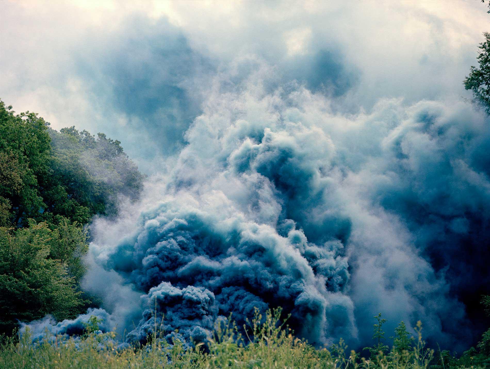 A big cloud of blue smoke filling a green field of grass