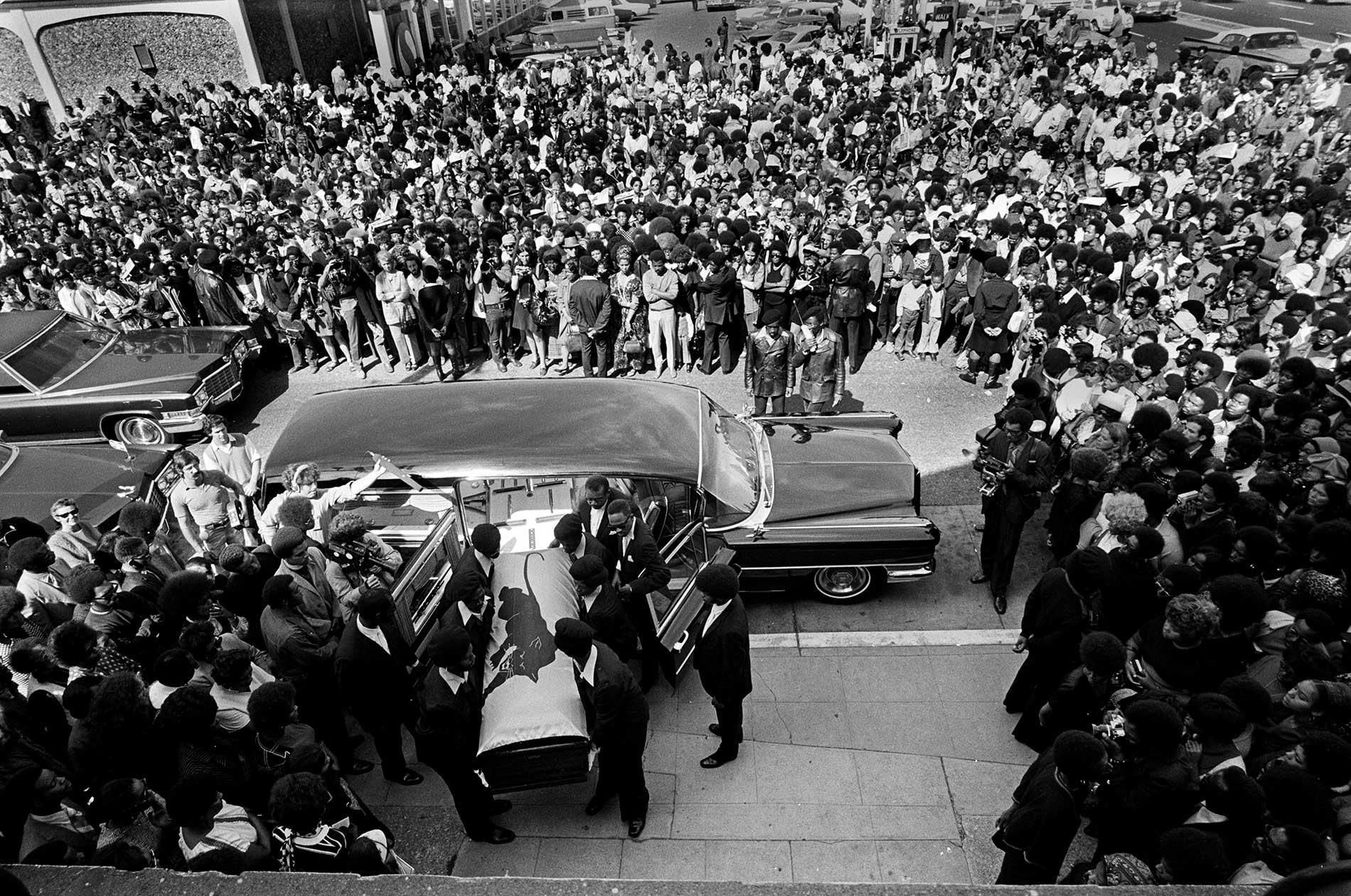 A crowd of people surrounding a casket being carried into a car
