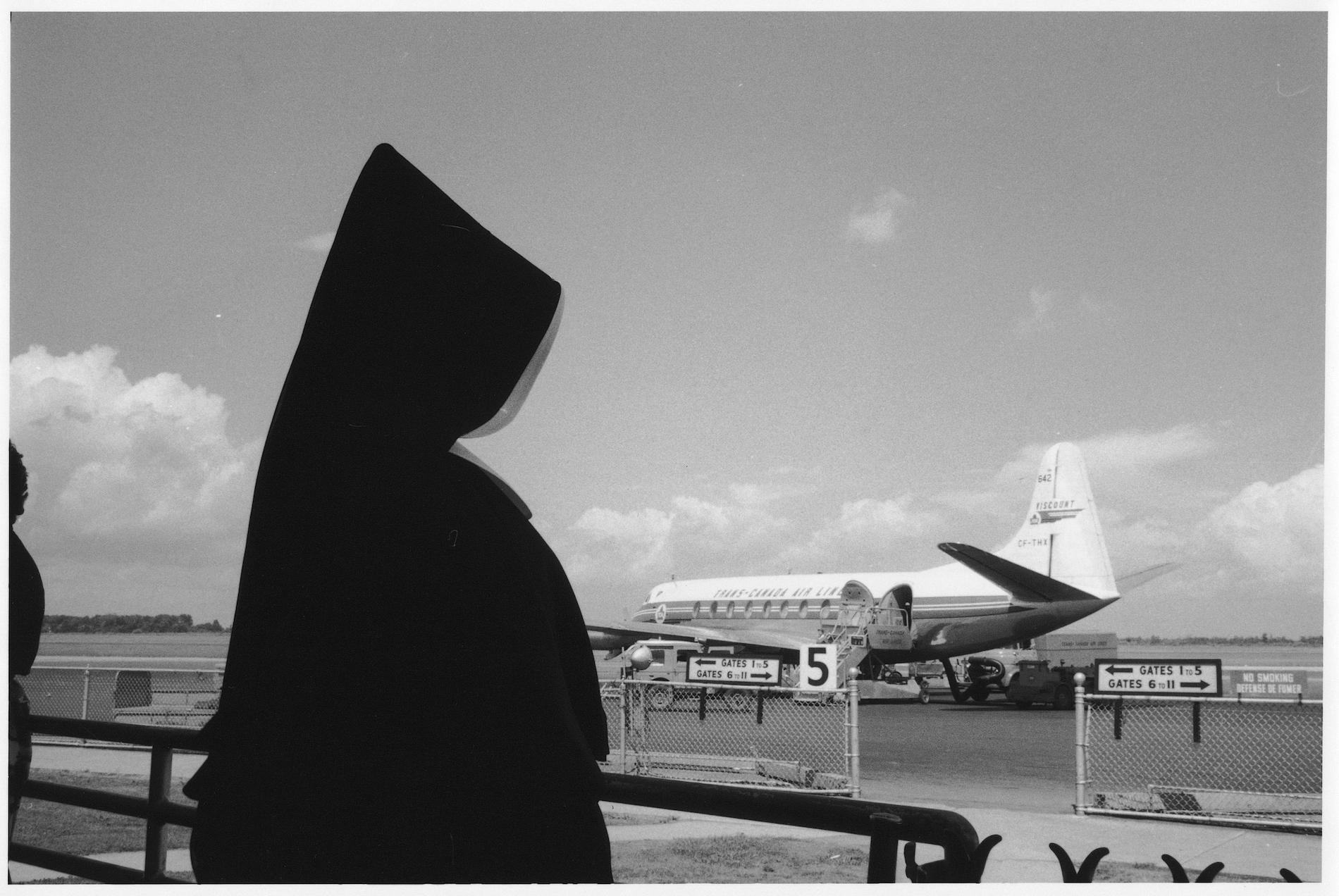 A nun dressed in black looks at an airplane on the runway
