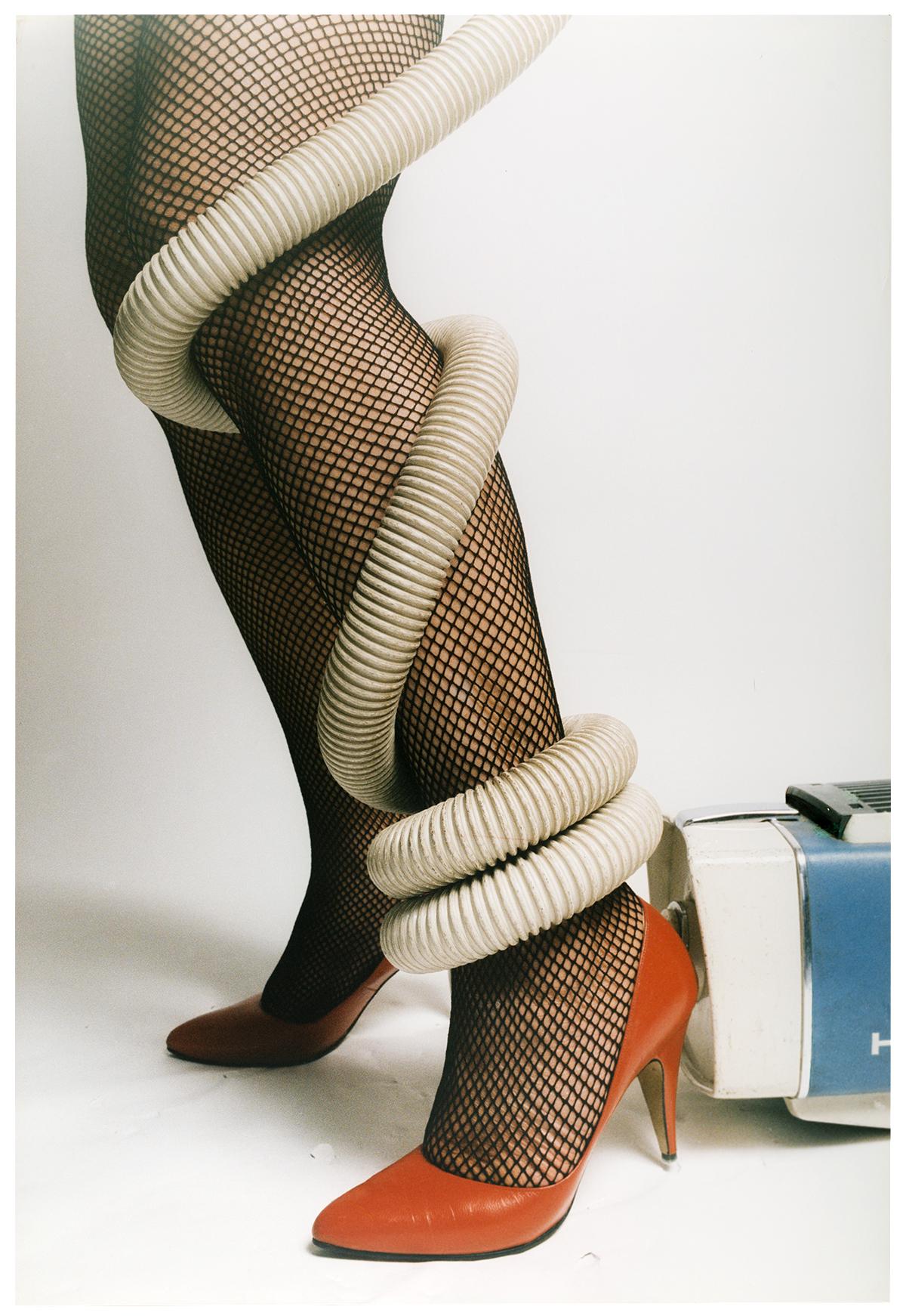 Photo of a vacuum hose wrapped around a woman's leg wearing fishnet stockings and orange heels.