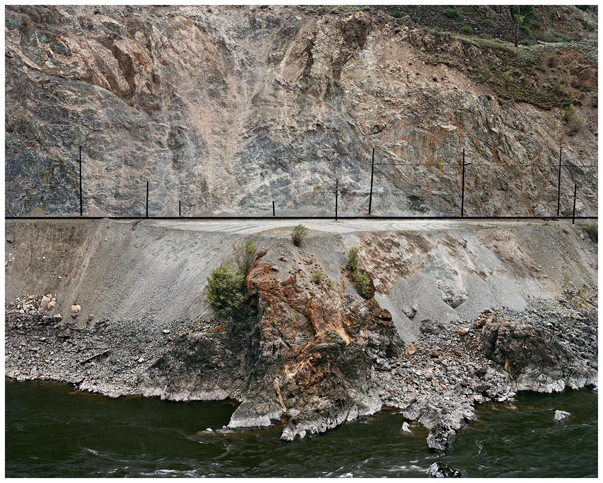 Photograph by Edward Burtynsky. A railway line cut into a mountain side.