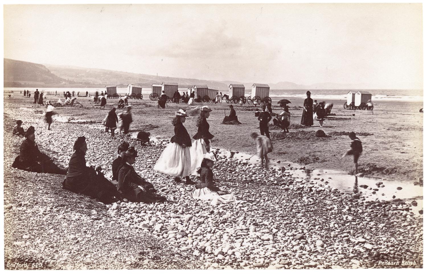 Groups of people gathered on a long stretch of rocky beach. Photograph by Francis Bedford.