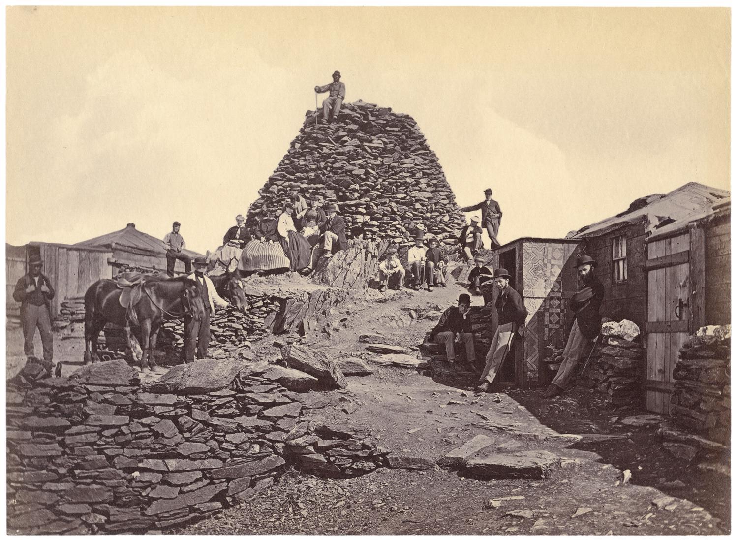 A group of people gathered around a small shelter and mounds of rocks. Black and white photograph by Francis Bedford.