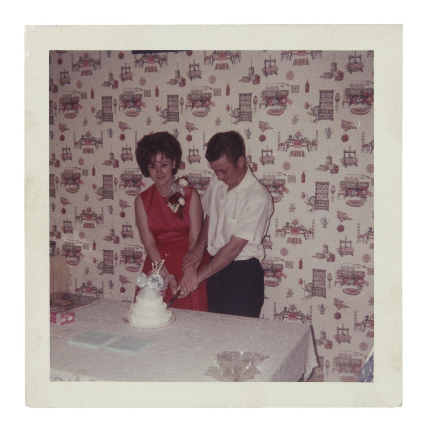man and woman cut a three-tiered wedding cake with hands clasped together.