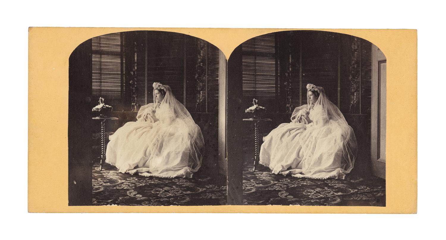 Bride in wedding dress sits to pose for a wedding in a carpeted room with blinds covering the window.