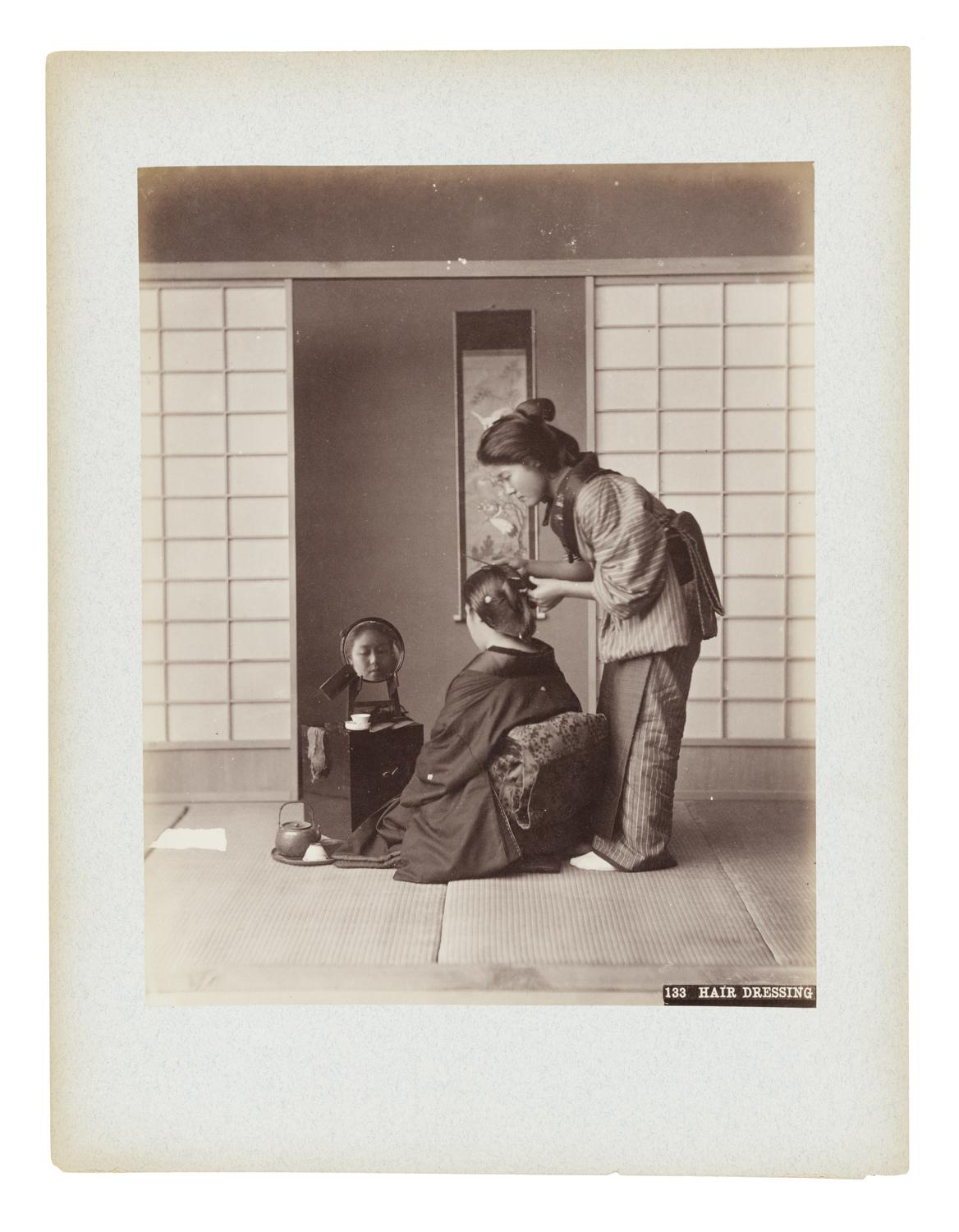 A seated woman has her hair done by another standing woman in Japan.