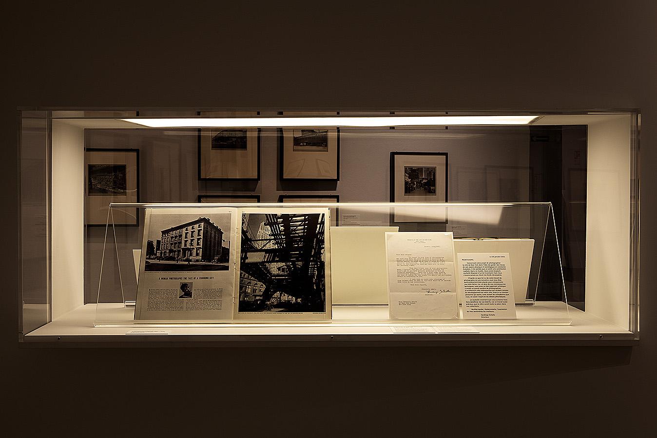 Old black and white documents sit in a glass case, lit from above