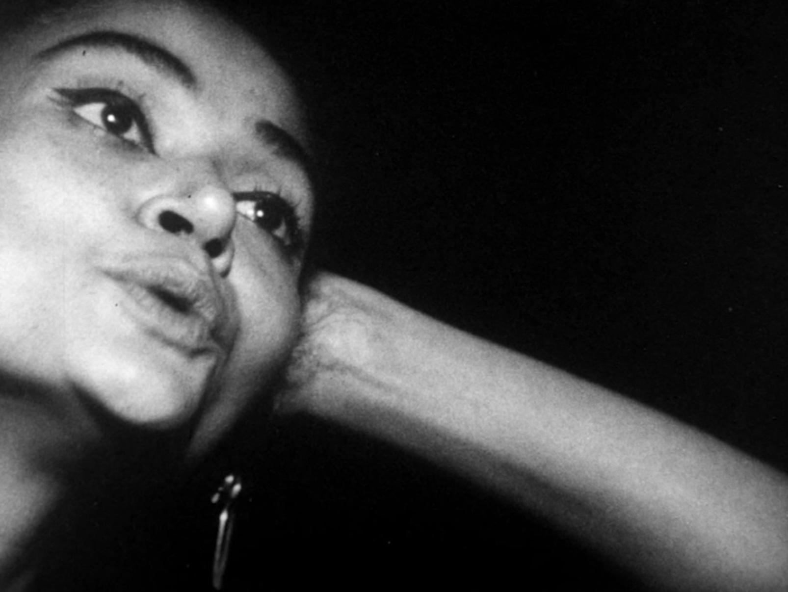 Black and white photo of women with her lips pursed with a slight opening while looking off into the distance. Black background. 2000w