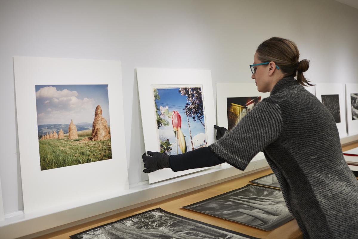 An individual places photographic artworks on a ledge for display.