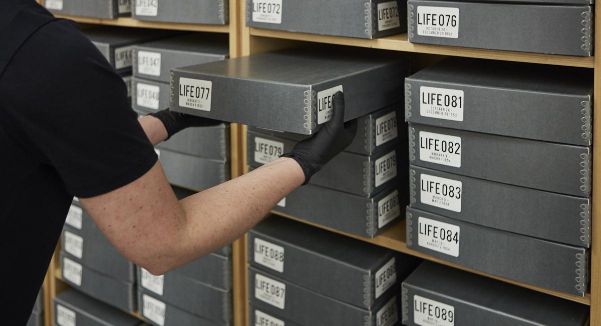 An archivist pulls a grey box labelled "Life" from a shelf