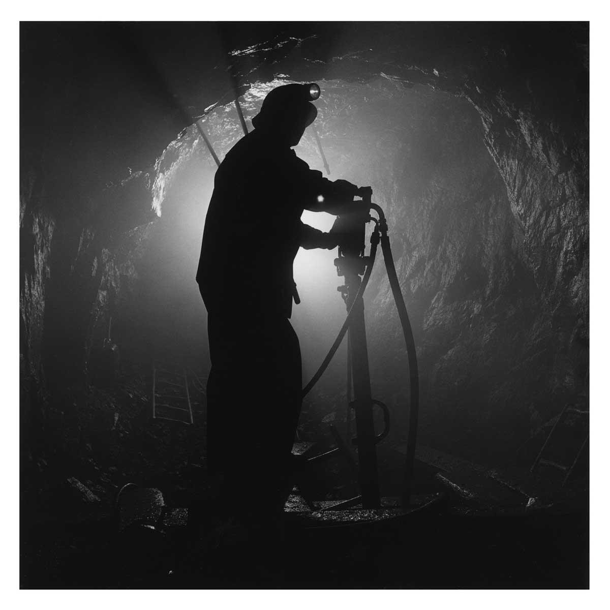 A black and white photo of a backlit miner working underground.