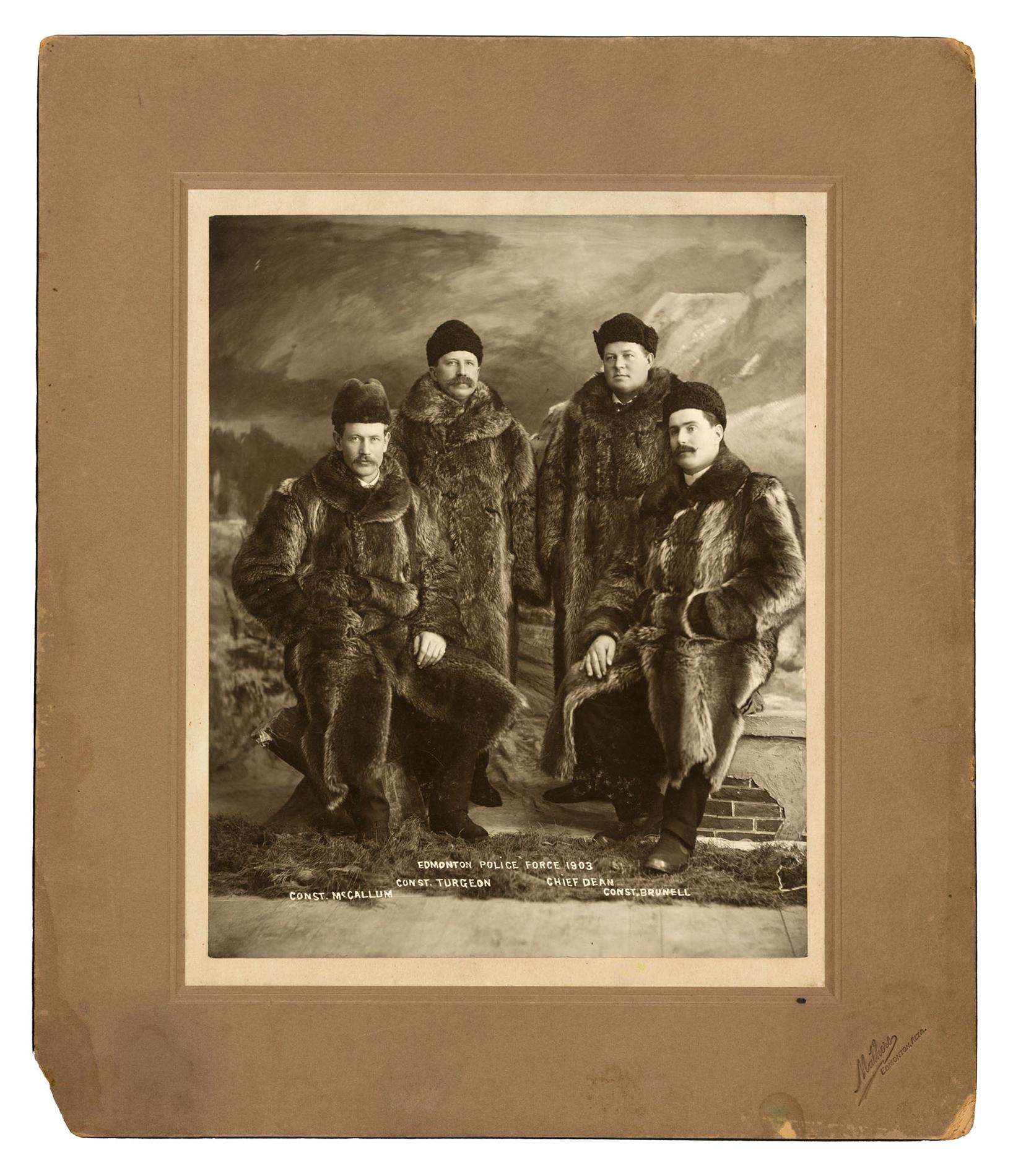 A formal studio portrait of four men in fur coats and hats