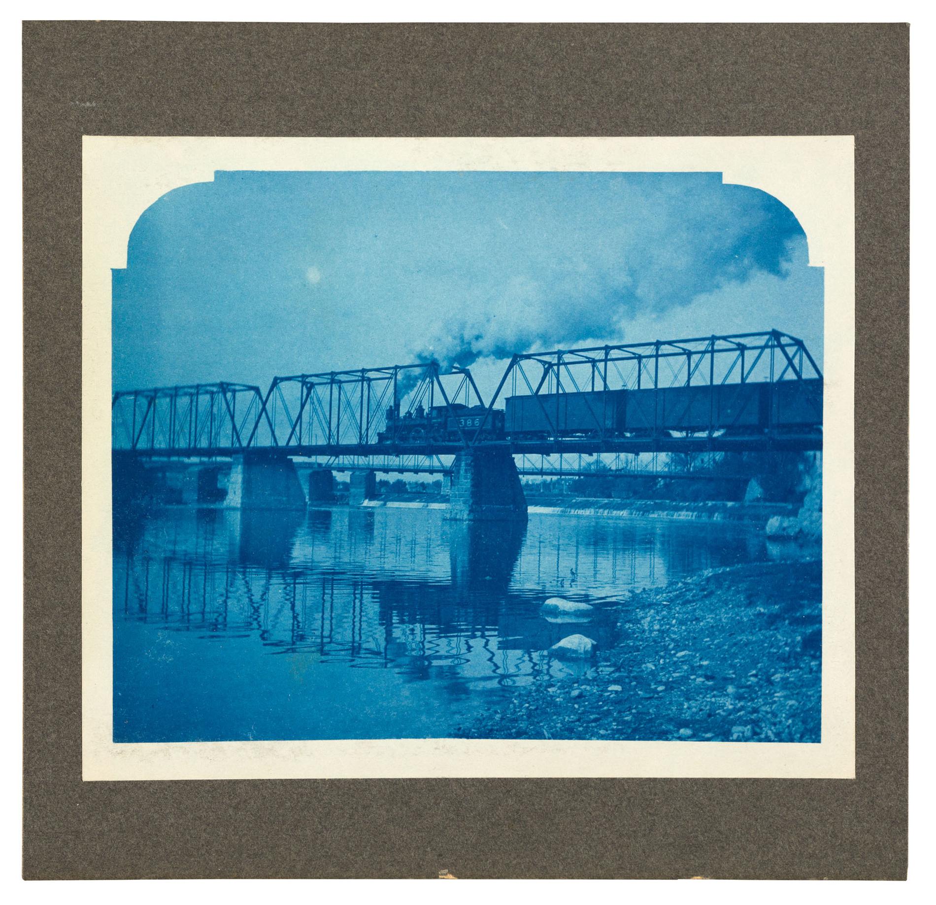 A blue-toned image of a train crossing a bridge over water