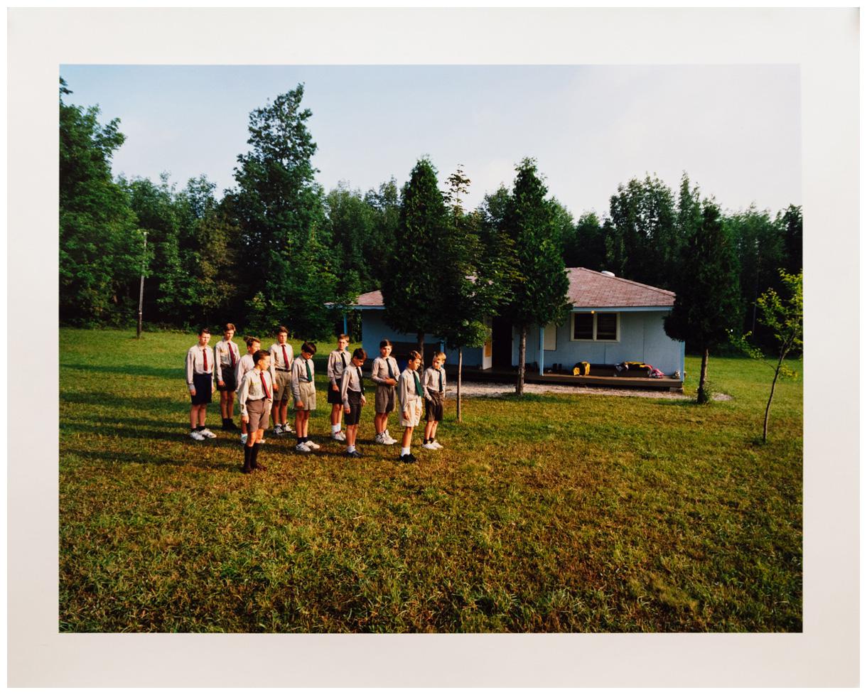 Photograph by Edward Burtynsky. Boys in uniform stand in formation outside a camp cabin