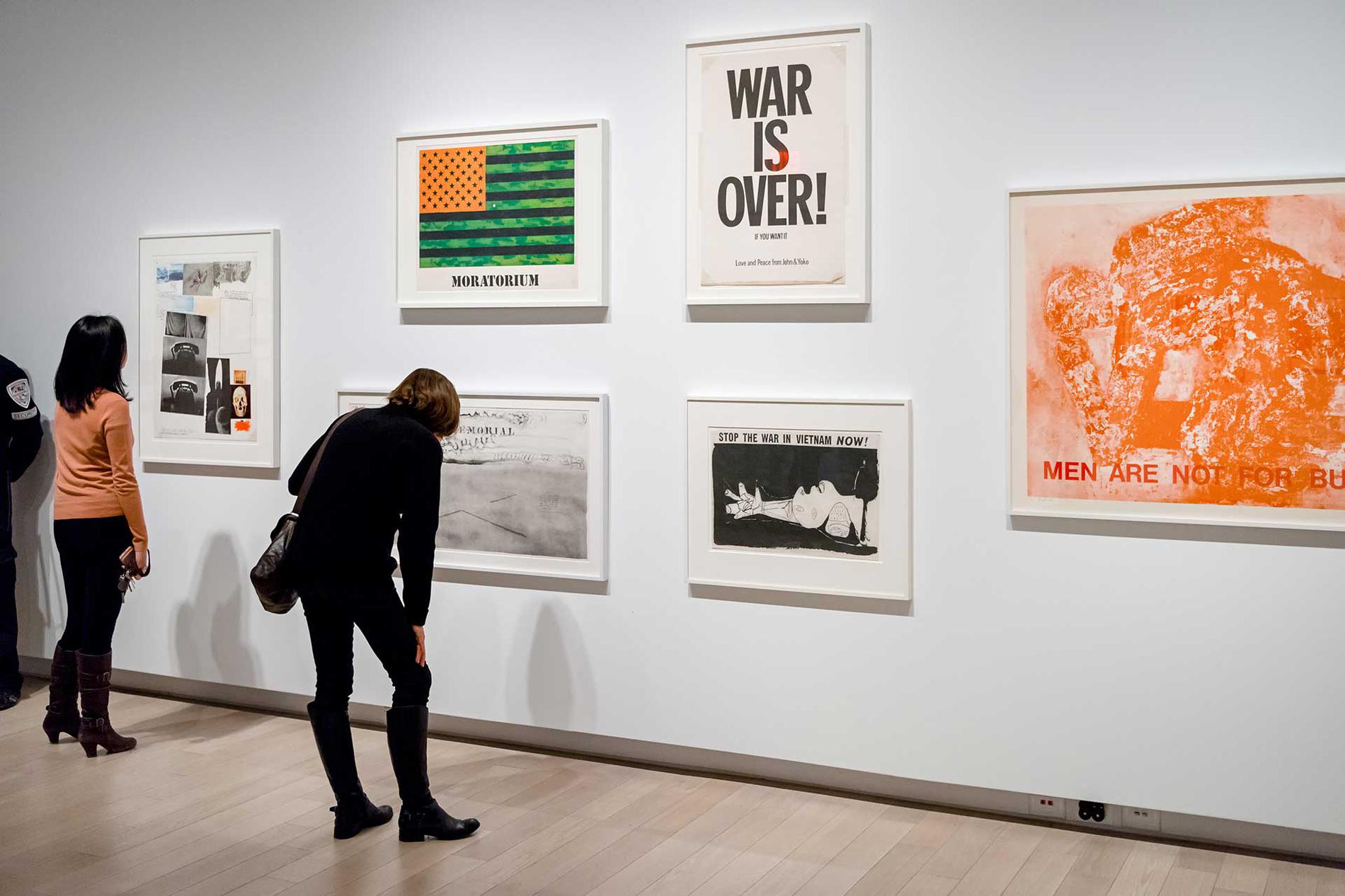 Two people looking at a wall in the gallery full of photographs and posters