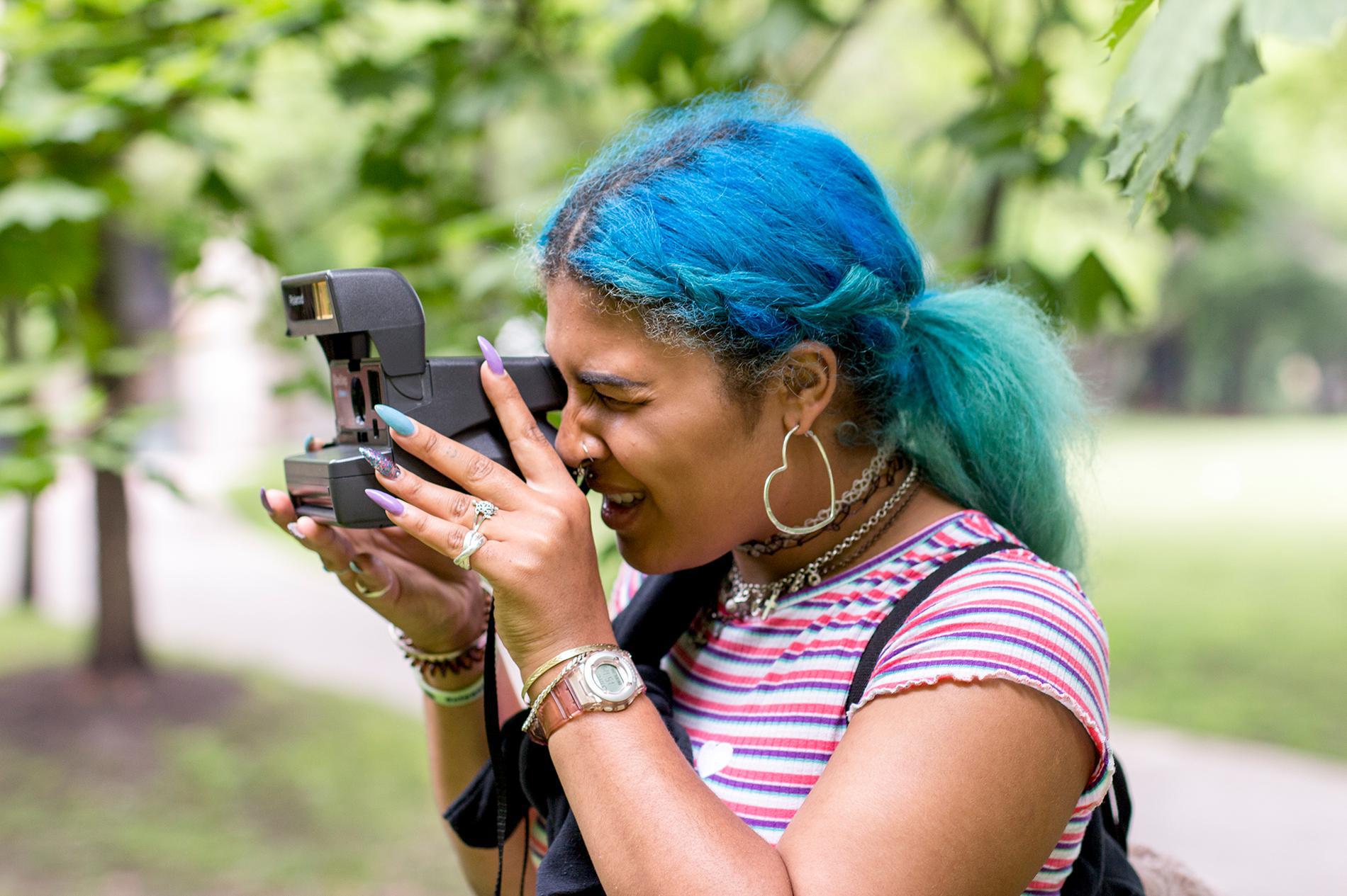 blue haired girl takes looks through viewfinder of polaroid camera