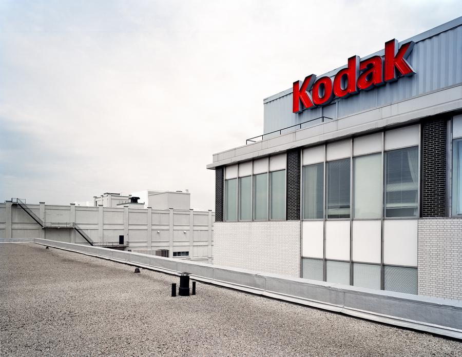 The roof of a building, an adjacent building has a red sign that reads 'Kodak'