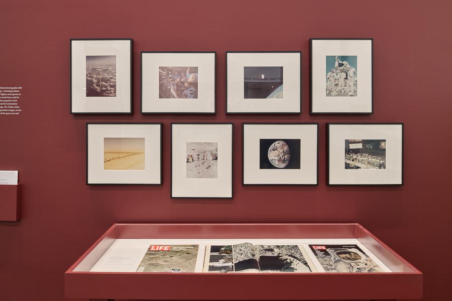 Eight framed colour photographs from NASA on a red gallery wall, above a red display vitrine at The Image Centre