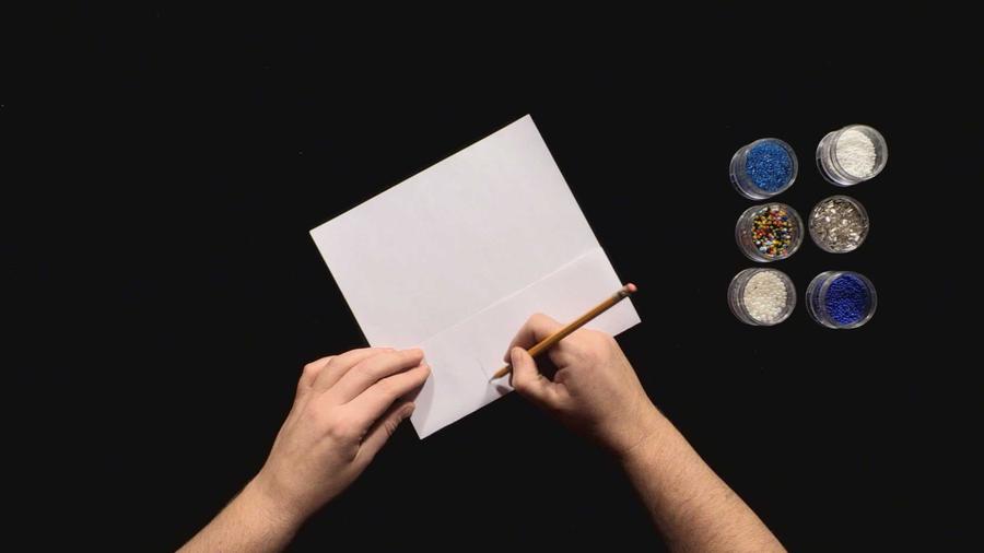 Hands writing on a piece of paper with a pencil, with jars of beads to the side