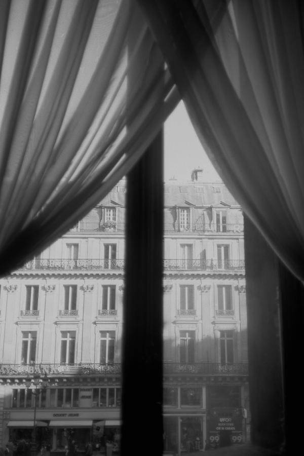 A 5 storey apartment building through a window, grey curtains hanging in the corners