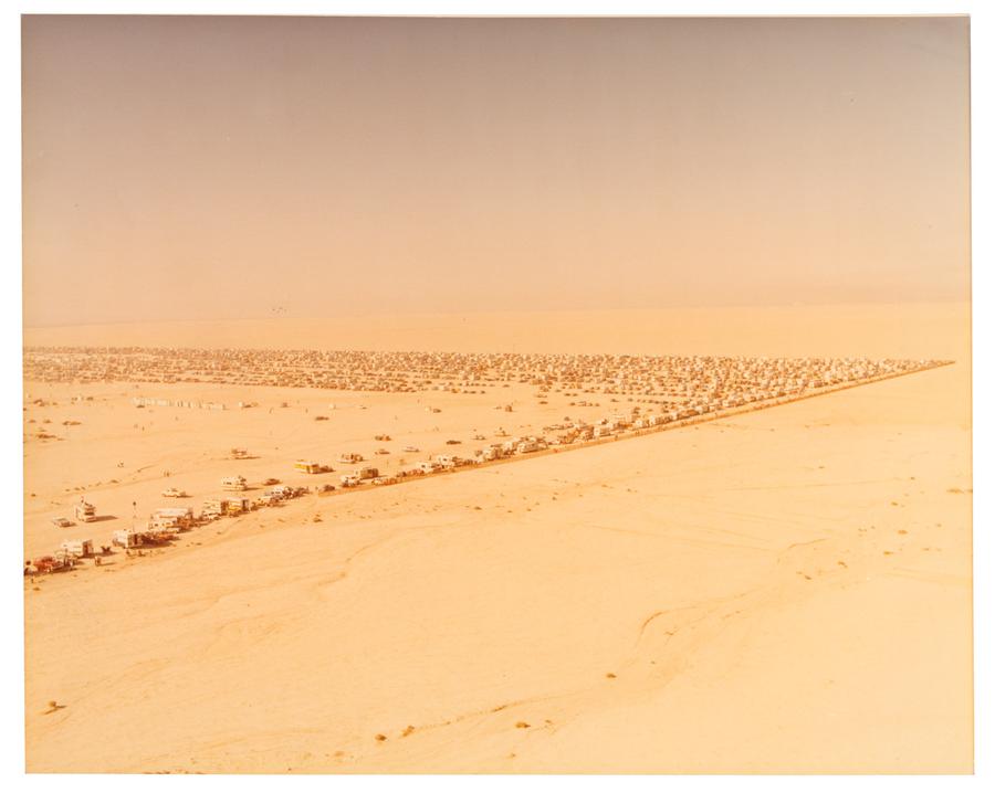 A desert landscape with many vehicles parked and lined up in a 90 degree angle