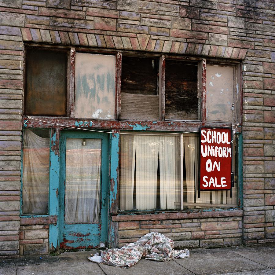 A rundown and abandoned storefront with a chipped blue door. Handpainted sign reads "school uniform on sale"
