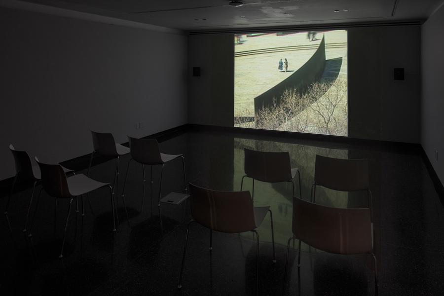 A projected video still of two people standing in a field of grass