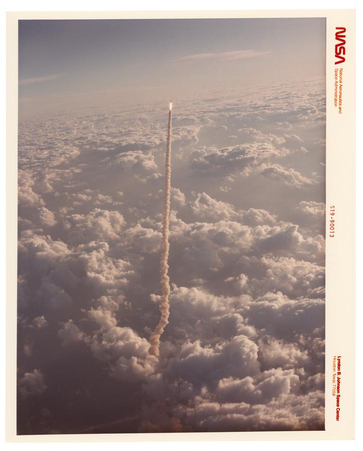 High above the clouds a spaceship flies vertically with a long trail of smoke behind it