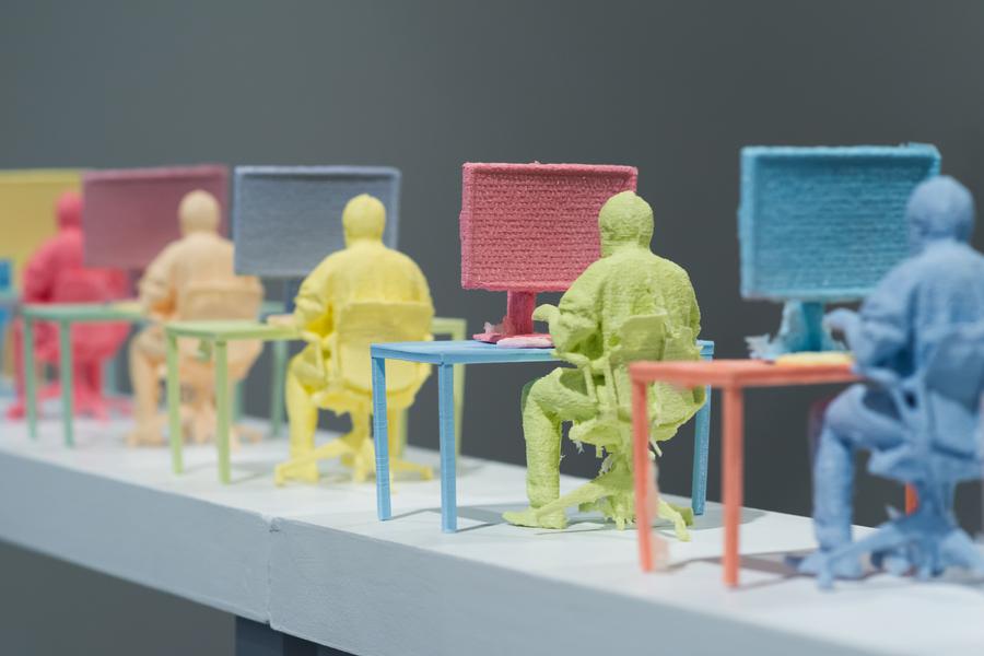 Close up of multiple miniature colourful figurines of men sitting at a desk with a computer