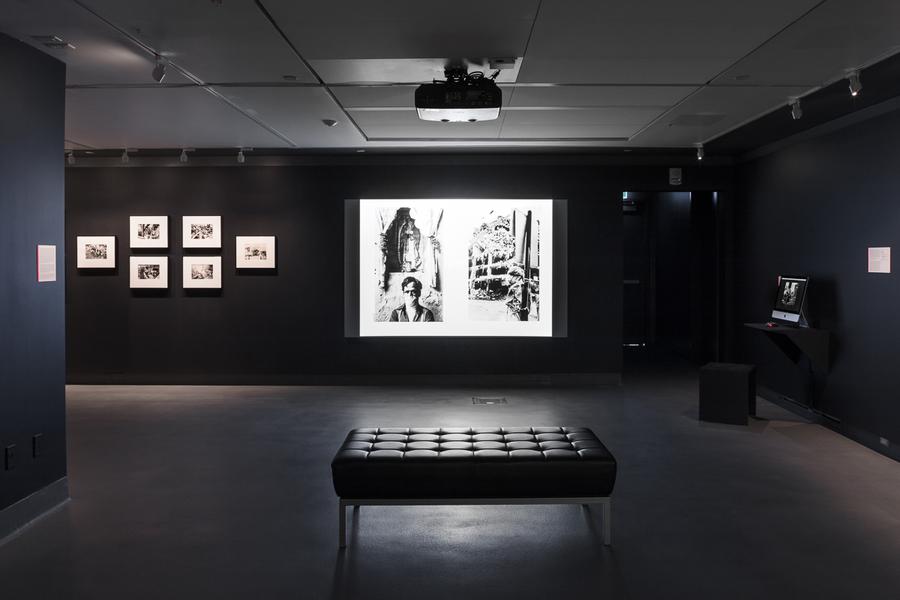 A gallery with black walls and photographs and a video projection
