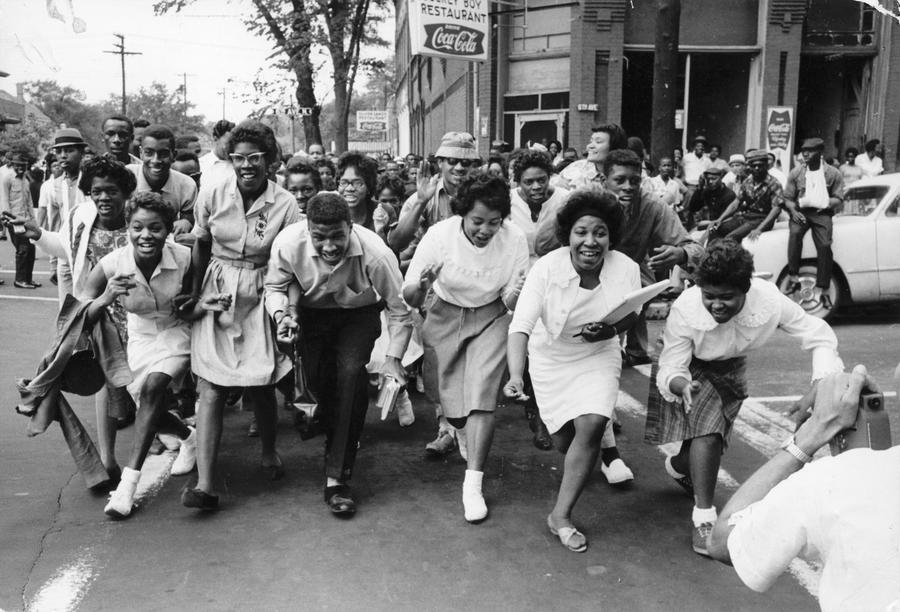 A group of young black men and women wearing white run across the street