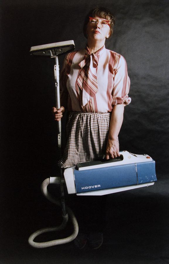 A woman wearing a striped blouse and skirt holds a vintage vacuum cleaner
