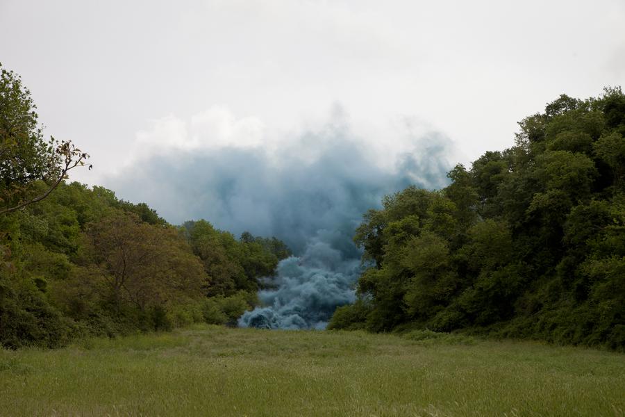 A big cloud of blue smoke filling a green field of grass