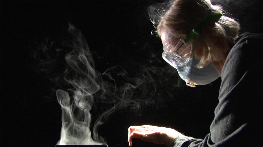 A woman wearing a mask as smoke rises in front of her