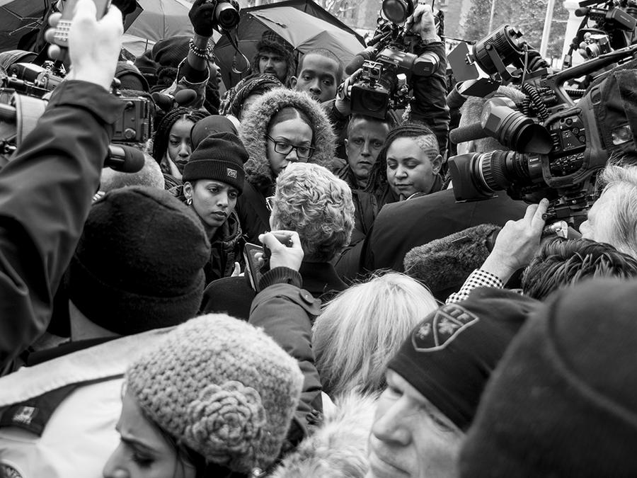 A large crowd of black people faces a crowd of white people, protest signage and media cameras raised