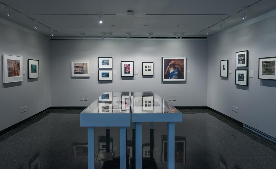 Two long display cases in the middle of the gallery, photographs on all three walls around it
