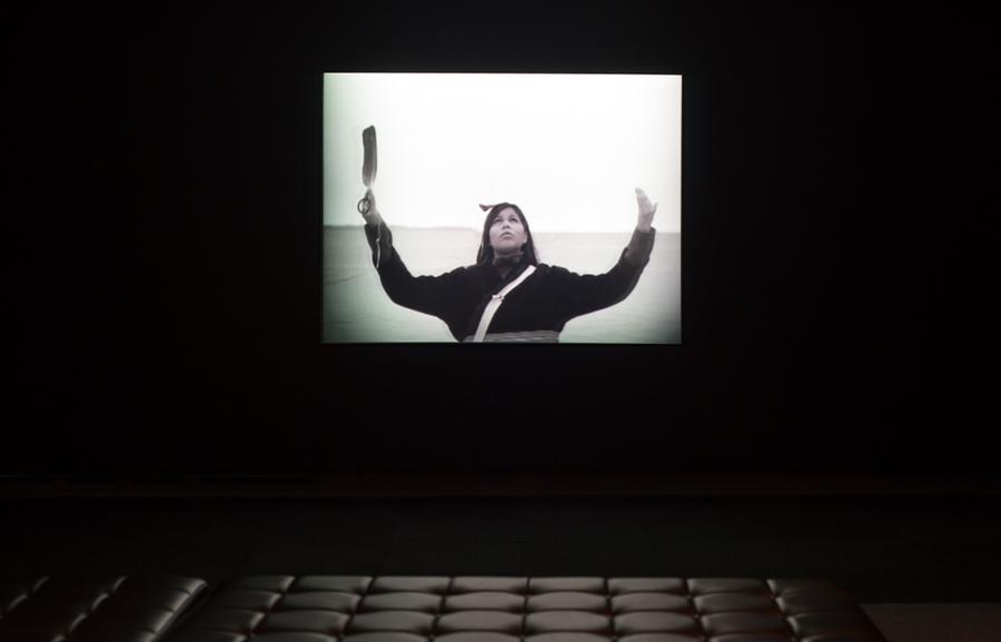 A film projected onto a dark wall featuring a woman holding her hands up in the air