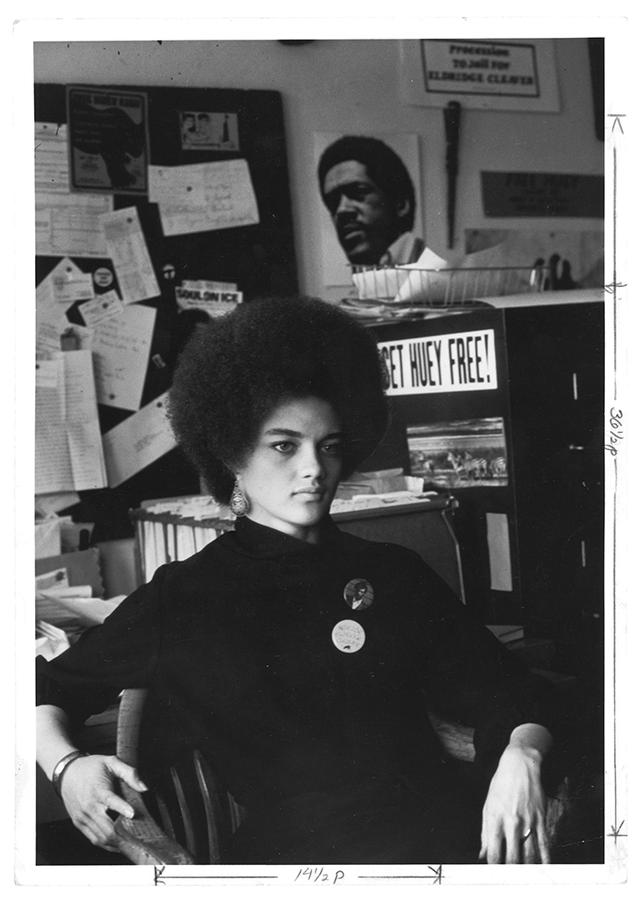 A woman in a black turtleneck sits at a desk