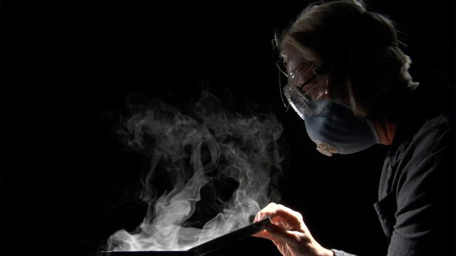 A woman wearing a mask as smoke rises in front of her