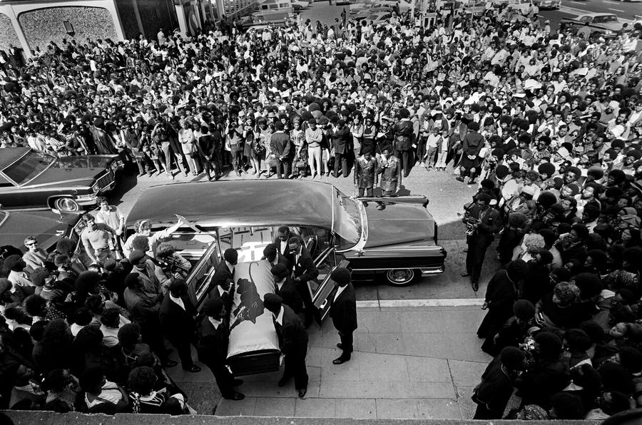 Large crowd of people watch as Black Panthers carry a coffin out of a hearse