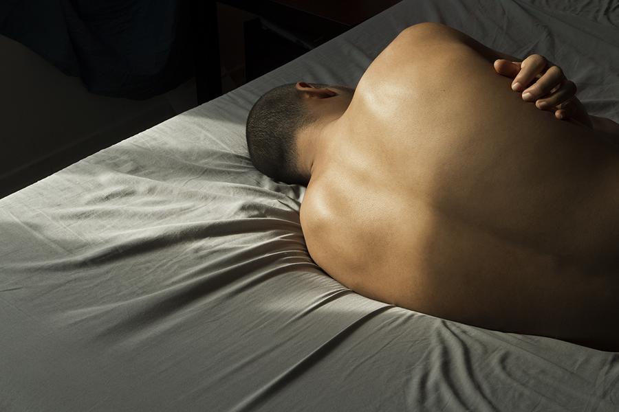 Shirtless man lying down, facing away