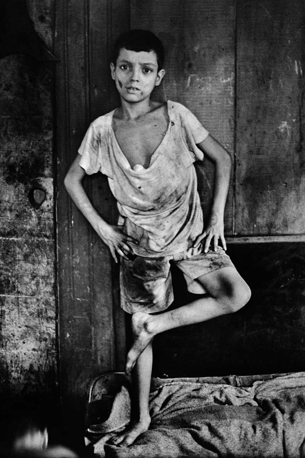 A boy posed against a wall in tattered clothing