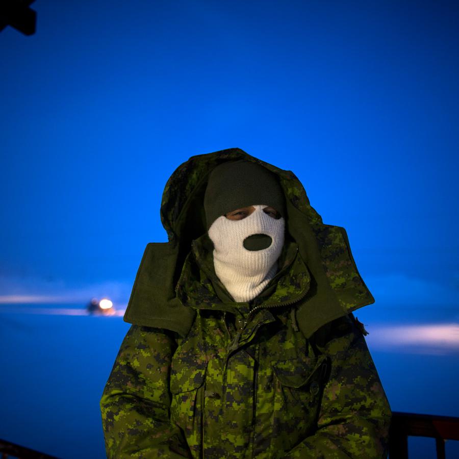 A portrait of a person outside at night in a white balaclava and a camo jacket