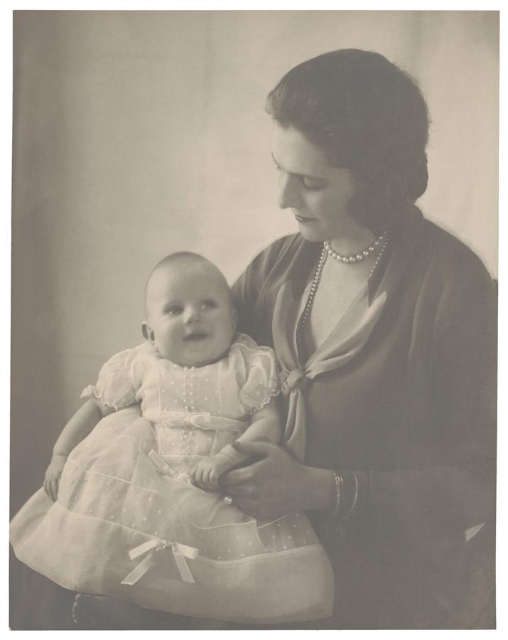 Studio portrait of a woman holding a baby, she looks at the baby while the baby smiles, looking up. Black and white photograph by Violet Keene Perinchief.