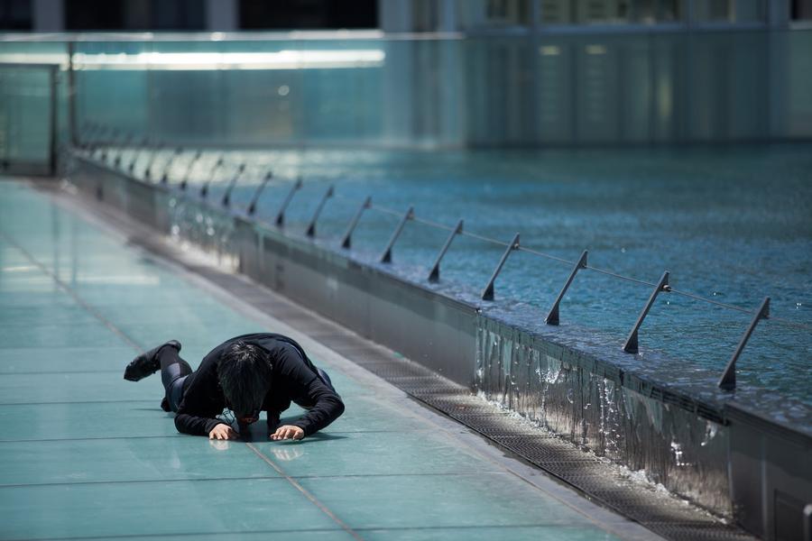 A figure dressed all in black crawls along the floor next to a pool of water.