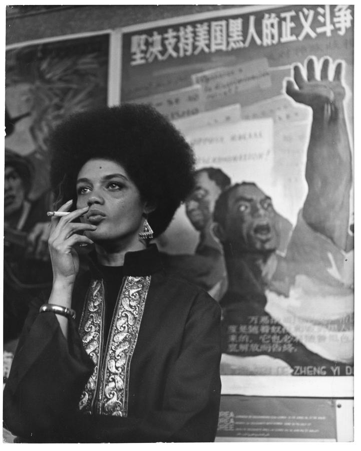 A woman smoking a cigarette, wearing a bracelet, earrings, and an intricate top